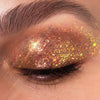 Geschlossenes Auge geschmückt mit dickem, glitzerndem und goldenem Lidschatten aus der Glorious Lights Glitter Palette, mit langen, dunklen Wimpern.
