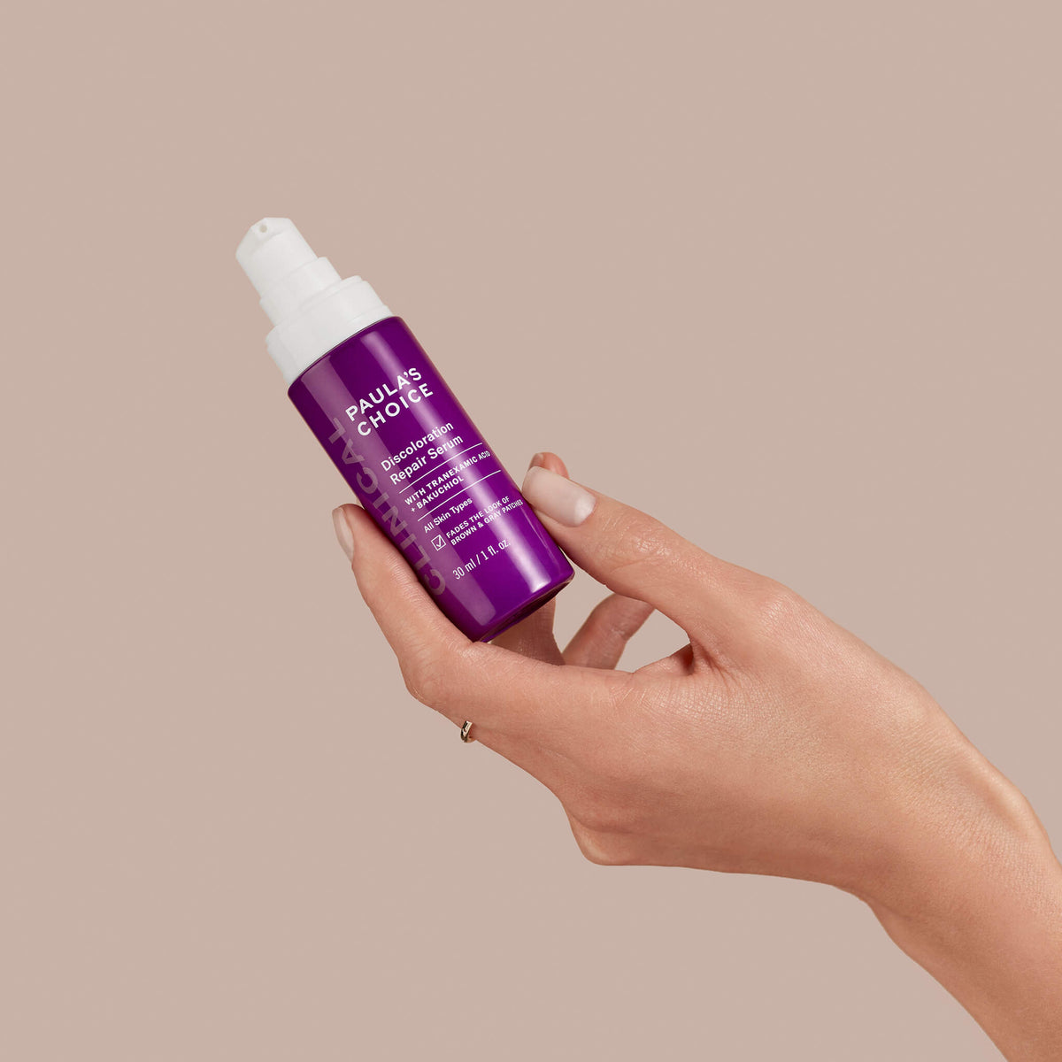 Eine Hand hält eine violette Flasche Paula's Choice Discoloration Repair Serum vor einem beigen Hintergrund.