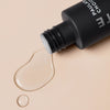 Eine geöffnete Flasche Skin Perfecting 2 % BHA Liquid Exfoliant Deluxe Mini von Paula’s Choice mit verschüttetem Produkt auf einer beigen Oberfläche.