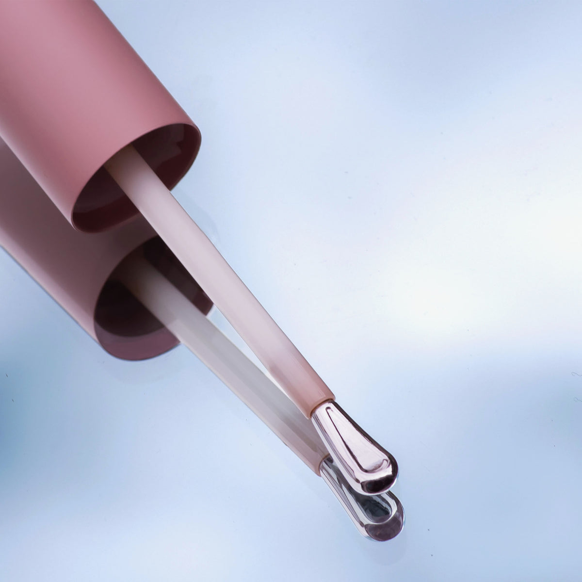 Nahaufnahme eines rosafarbenen Applikators des Wide Awake Full Coverage Concealer mit silberner Spitze vor hellem Hintergrund, gespiegelt auf glatter Oberfläche.