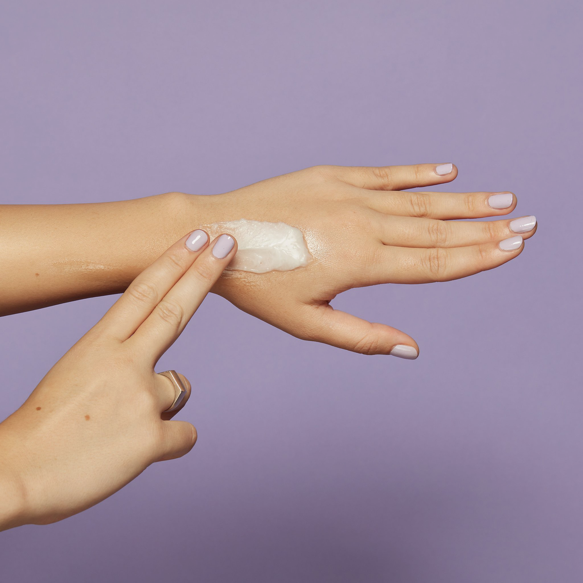 Nahaufnahme der Hände einer Person vor violettem Hintergrund; die den Clean It Zero Cleansing Balm Purifying auf ihren Handrücken aufträgt