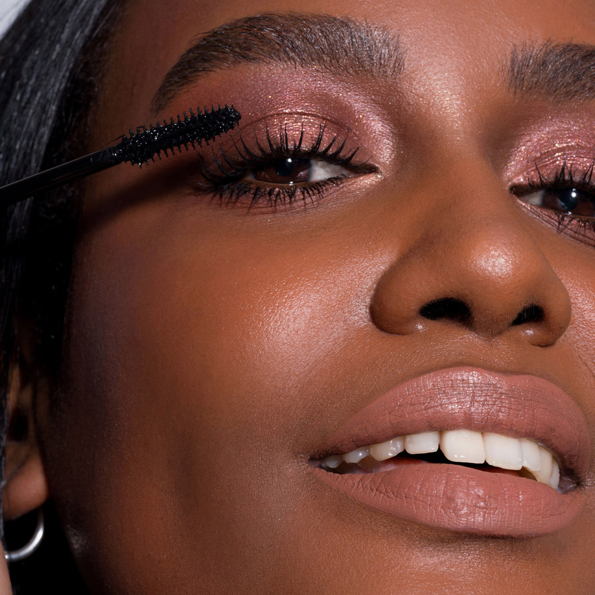 Nahaufnahme einer Frau, die LH Cosmetics Infinity Power Lash Soft Volume Mascara auf ihre oberen Wimpern aufträgt.
