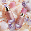 Zwei rosa getönte NABLA Angel Aura-Flaschen mit sichtbaren Deckeln und Pumpen auf rosa und violetten Kristallen und Salz.