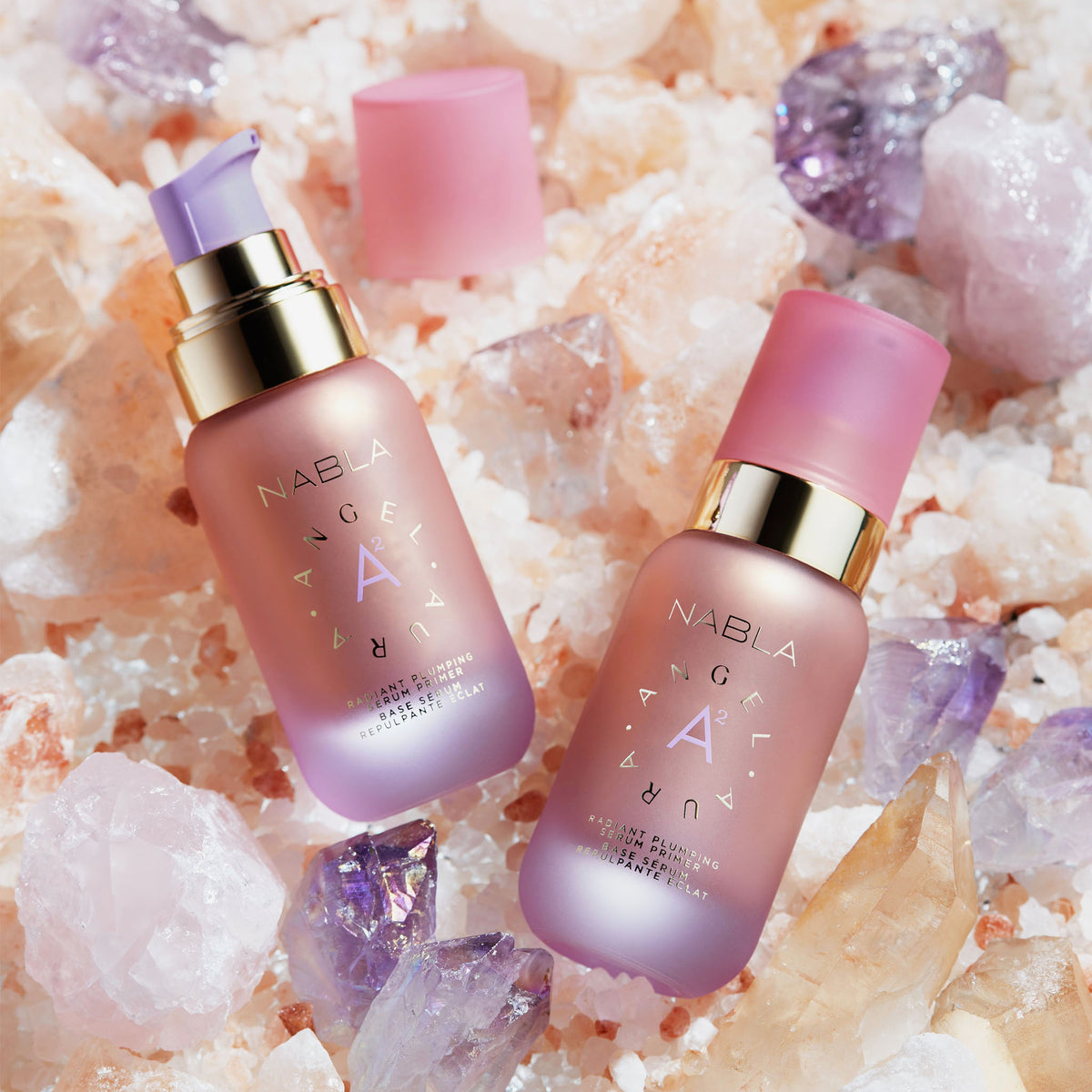 Zwei rosa getönte NABLA Angel Aura-Flaschen mit sichtbaren Deckeln und Pumpen auf rosa und violetten Kristallen und Salz.