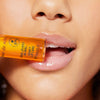 Nahaufnahme eines Mundes mit glänzenden, gepflegten Lippen. Die Person hält das NUXE Rêve de Miel Honey Lip Care Öl leicht zwischen den Lippen.