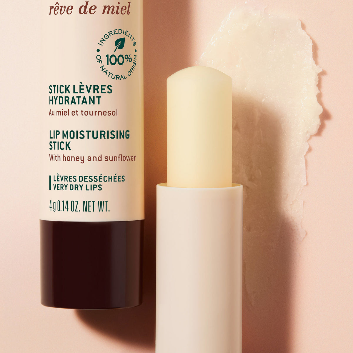 NUXE Rêve de Miel Lippenpflegestift mit aufgedrehter Spitze, daneben die Verpackung mit Text und einem Auftrag des Stifts auf rosafarbenem Hintergrund.