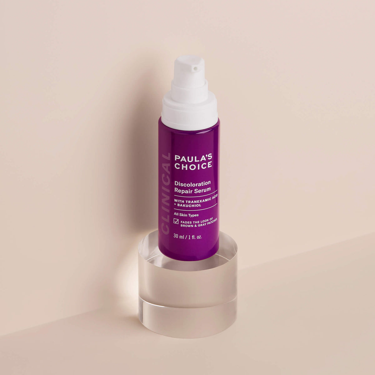 Lila Pumpspender des Paula’s Choice Discoloration Repair Serums mit weißem Deckel, stehend auf transparentem Podest vor beigem Hintergrund.