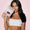 Frau mit weißem Top hält eine Verpackung des Loving Tan Deluxe Applicator Mitts in der einen Hand und trägt den schwarzen Bräunungshandschuh an der anderen.