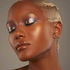 Person mit geschlossenen Augen und dunklem Hautton präsentiert schimmernden, irisierenden Make-up-Look mit den Infinite Chrome Flakes.