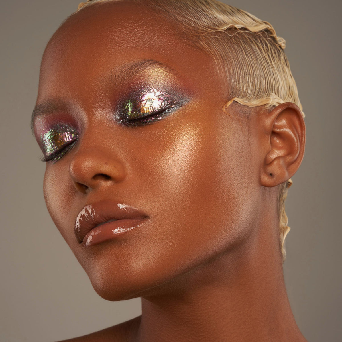 Person mit geschlossenen Augen und dunklem Hautton präsentiert schimmernden, irisierenden Make-up-Look mit den Infinite Chrome Flakes.