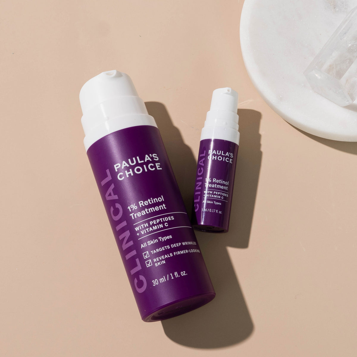 Zwei Flaschen Clinical 1 % Retinol Treatment werden auf einer beigen Oberfläche mit einer weißen Schale präsentiert.