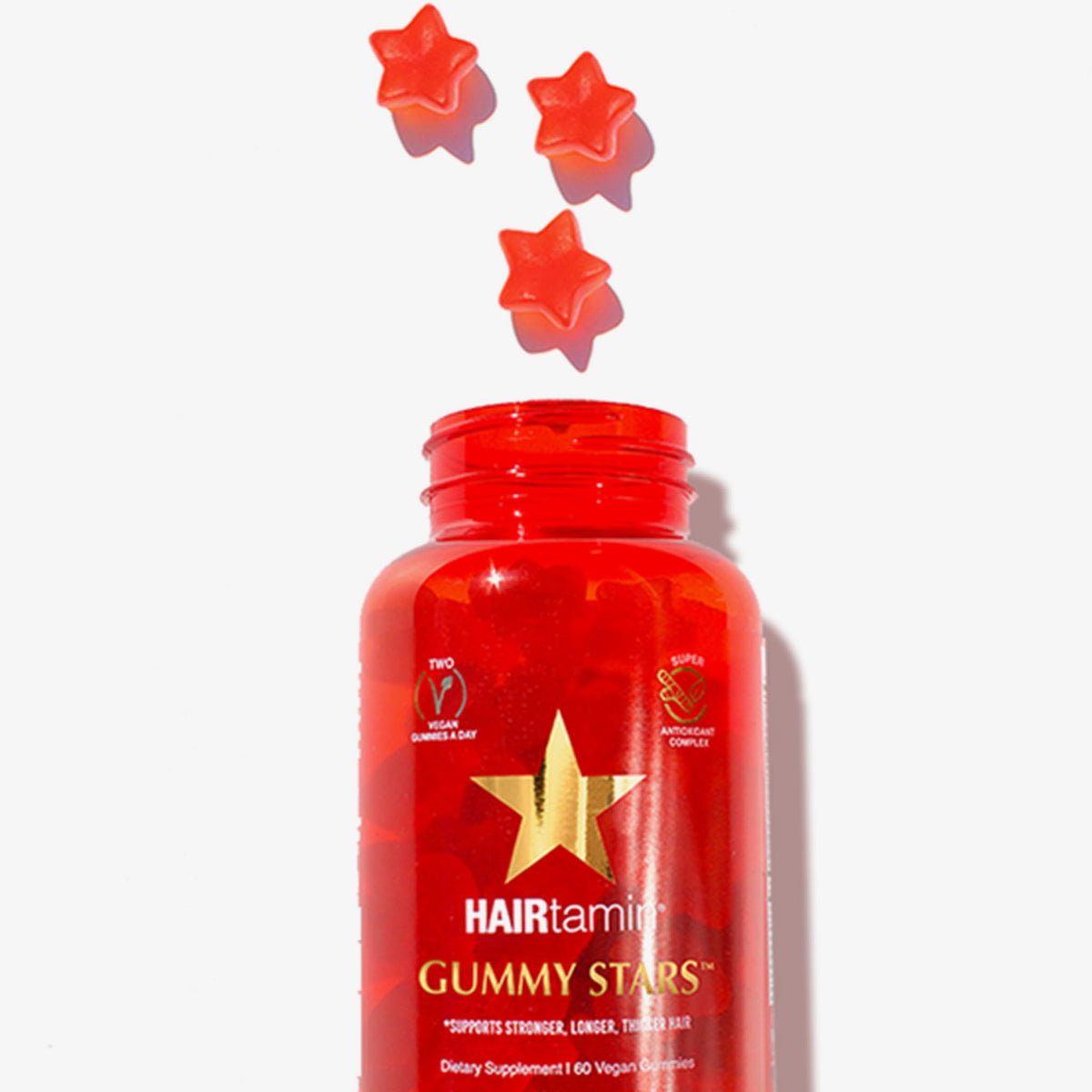 Offene Packung HAIRtamin Gummy Stars™ aus der 3 Stars herausgefallen sind. Weißer Grund.