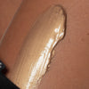 Nahaufnahme eines bronzefarbenen Creme-Swatches auf gebräunter Haut, mit sichtbarem Schimmer und seidiger Textur.