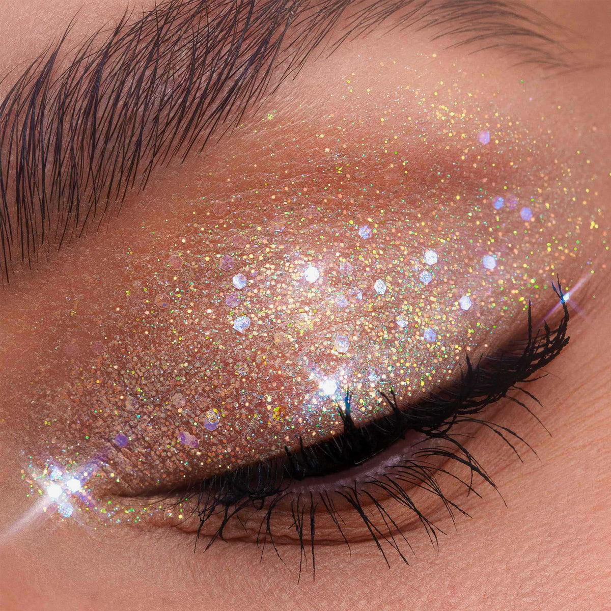 Ein geschlossenes Auge präsentiert lange, dunkle Wimpern und schimmerndes Weiß mit Glitzerlidschatten aus der Glorious Lights Glitter Palette.