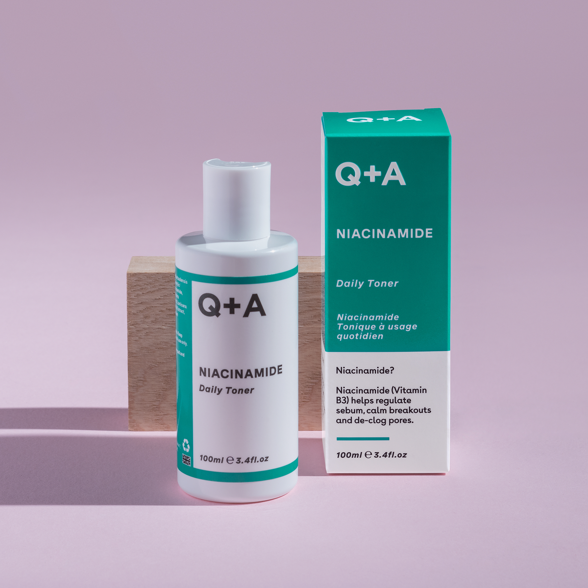 Eine Flasche und eine Schachtel Niacinamide Daily Toner 100 ml, präsentiert auf einem rosa Hintergrund mit einem Holzblock.