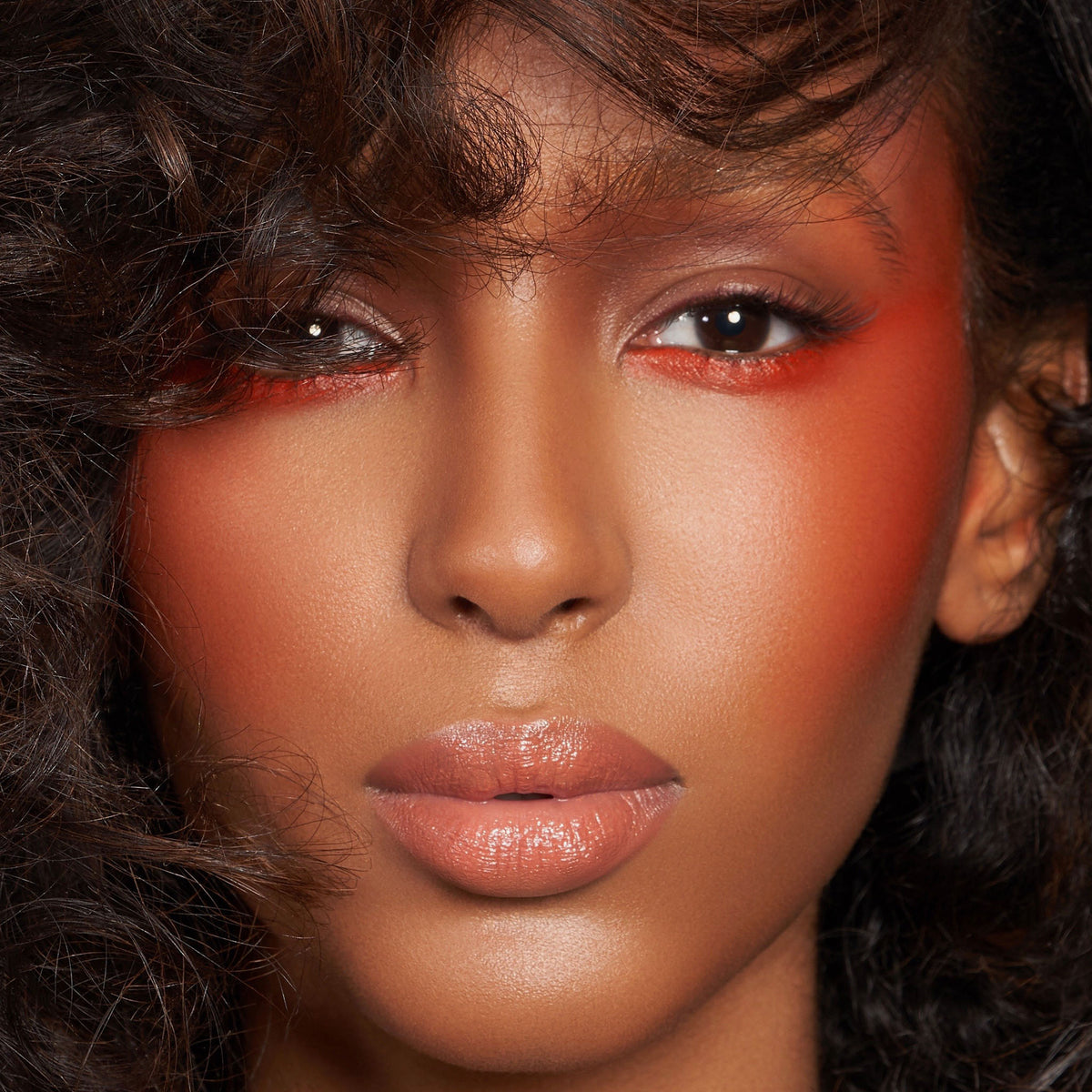 Eine Frau mit kräftigem orangefarbenem Lidschatten und Rouge, glänzenden Lippen und voluminösem lockigem Haar, kreiert mit der Waterproof Cream Palette.