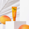 Eine Tube Bondi Sands Lip Balm SPF 50+ in Orange steht auf einem weißen Sockel, umgeben von Mangos