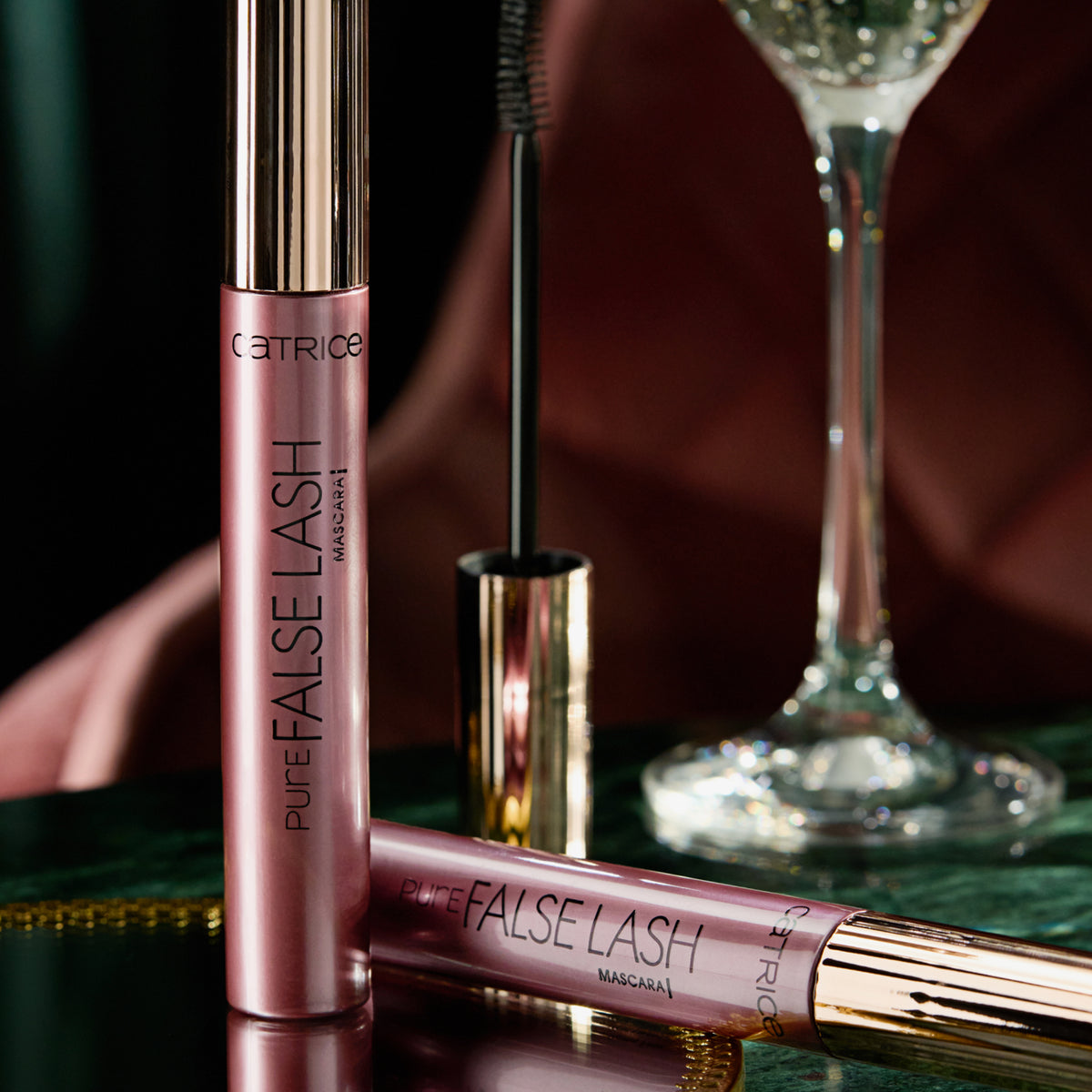 Zwei Tuben Catrice Cosmetics Pure False Lash Mascara 010 in eleganter dunkler Umgebung mit Sektglas.