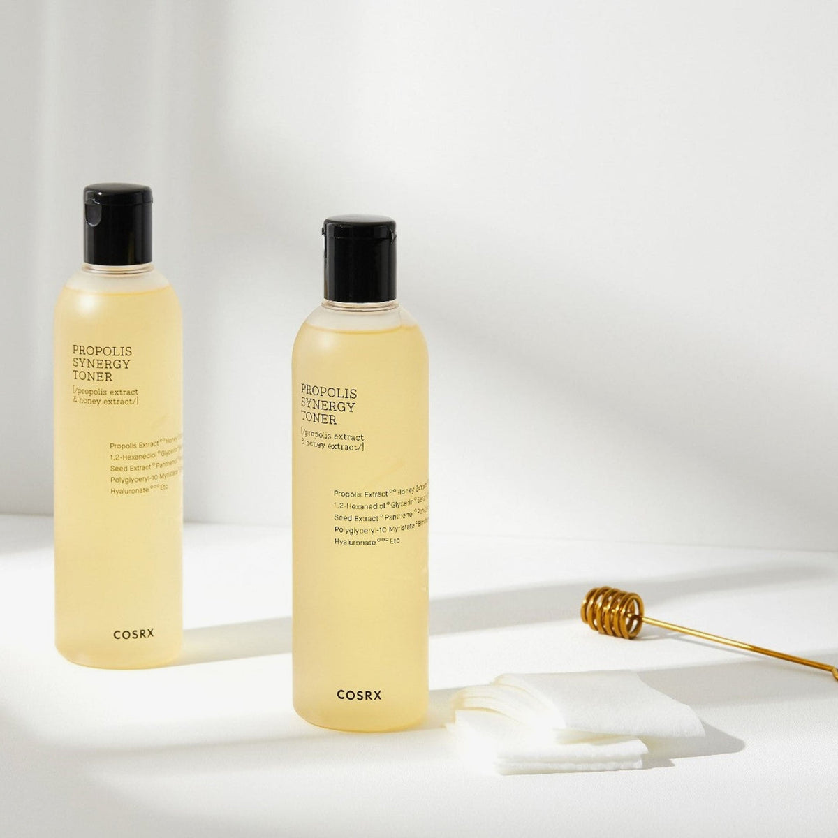 Zwei Flaschen Full Fit Propolis Synergy Toner werden mit Wattepads und einem Honiglöffel auf einer weißen Oberfläche präsentiert.