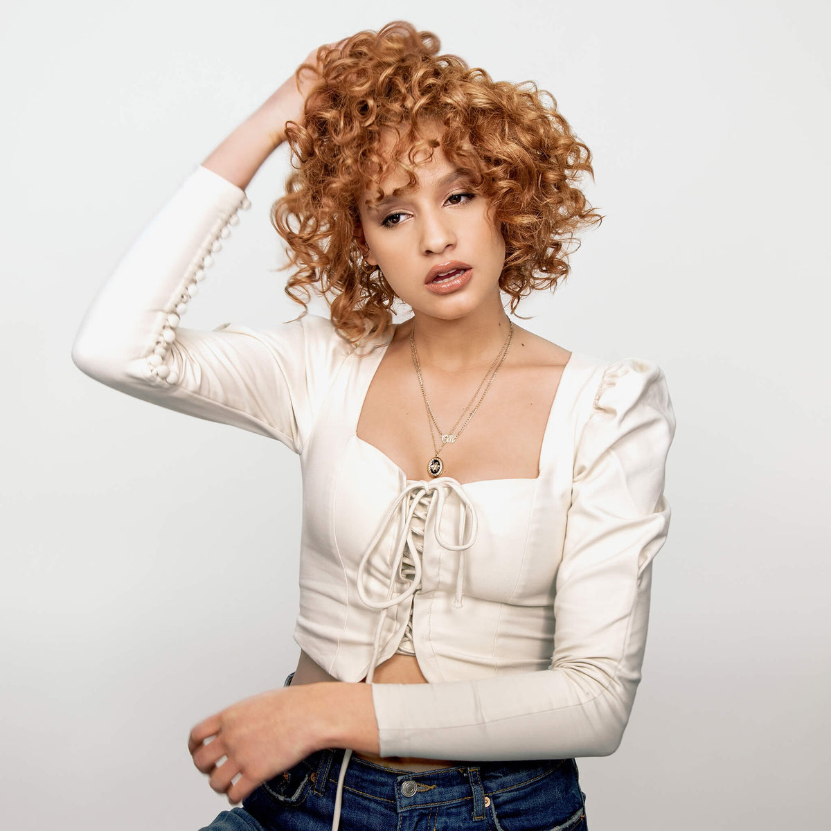 Eine Frau mit lockigem rotem Haar zeigt Wirkung des Dream Coat For Curly Hair vor weißem Hintergrund.