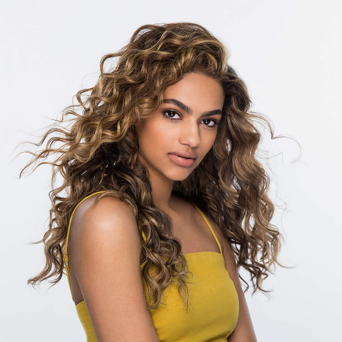 Frau mit langen glänzenden, definierten Locken präsentiert Wirkung des Dream Coat For Curly Hair vor einem hellen Hintergrund.