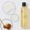 Eine Flasche Full Fit Propolis Synergy Toner mit Honig, Wattepads und Petrischalen auf einer weißen Oberfläche.