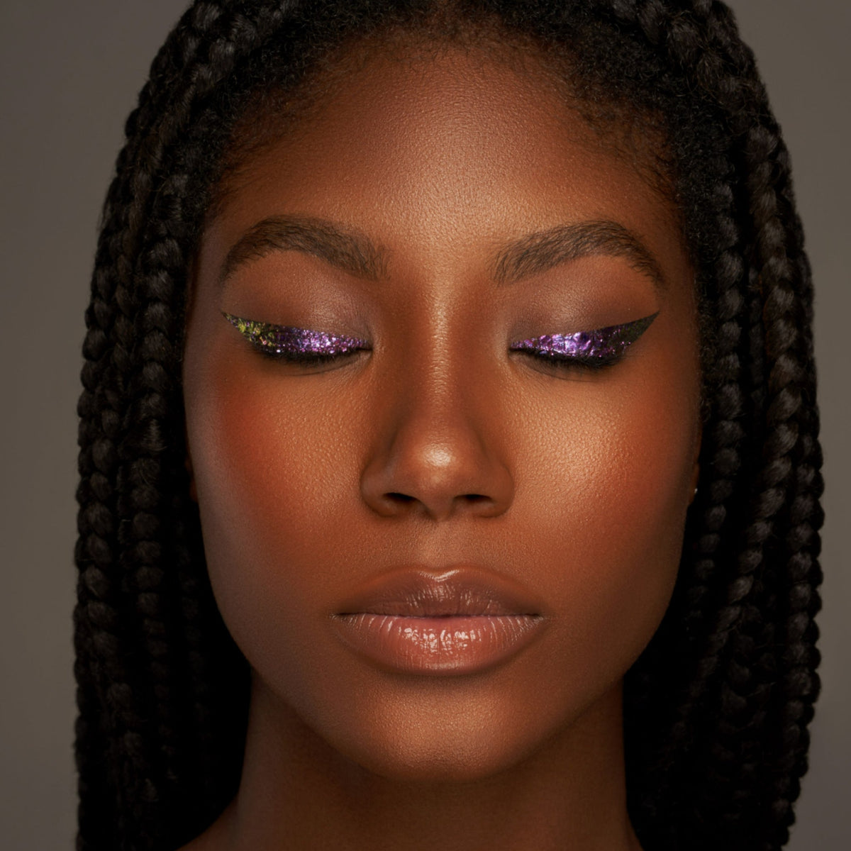 Person mit geschlossenen Augen und dunklem Hautton präsentiert schimmernden, irisierenden Make-up-Look mit den Infinite Chrome Flakes.