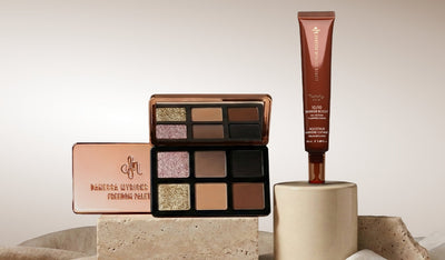 Geöffnete Lidschattenpalette mit warmen Nude- und Schimmertönen neben braunem Hautpflege-Tube auf Podesten.