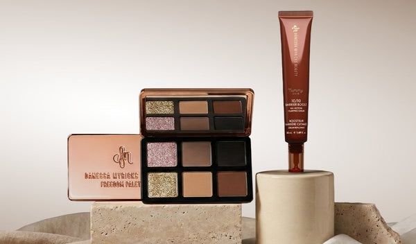 Geöffnete Lidschattenpalette mit warmen Nude- und Schimmertönen neben braunem Hautpflege-Tube auf Podesten.