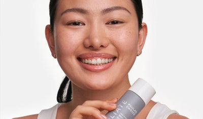 Lächelnde Frau hält ein Hautpflegeprodukt für Fruchtsäurepeeling vor ihr Gesicht.