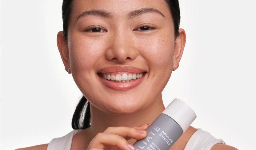 Lächelnde Frau hält ein Hautpflegeprodukt für Fruchtsäurepeeling vor ihr Gesicht.