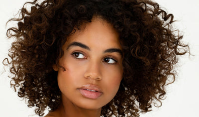 Frau mit natürlichen Locken und definierter Curly Hair Frisur blickt seitlich in die Kamera.
