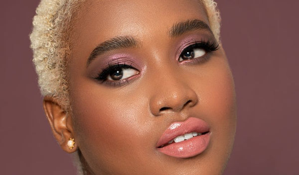 Frau mit kurzem blondem Haar, rosa Lidschatten, Wing-Eyeliner und glänzenden Lippen in Nahaufnahme.