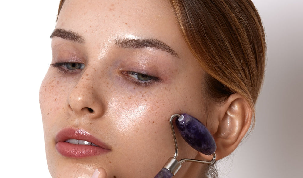 Frau massiert ihr Gesicht mit einem lilafarbenen Gesichtsroller und zeigt glatte, strahlende Haut.