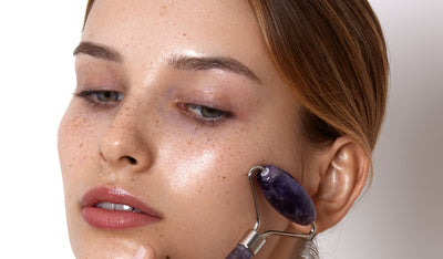 Frau massiert ihr Gesicht mit einem lilafarbenen Gesichtsroller und zeigt glatte, strahlende Haut.