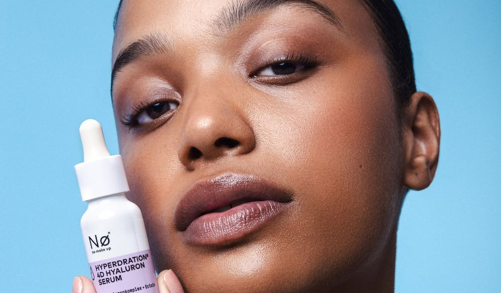 Frau mit glowy Haut hält ein Hyaluron-Serum von Nø Cosmetics vor ihr Gesicht und blickt selbstbewusst in die Kamera.