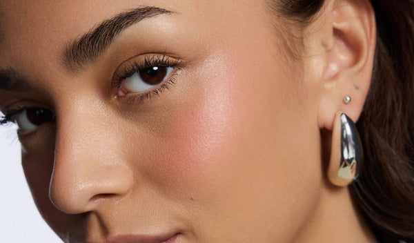 Nahaufnahme eines Gesichts mit rosigem Blush, natürlichem Glow und silbernem Creolen-Ohrring.