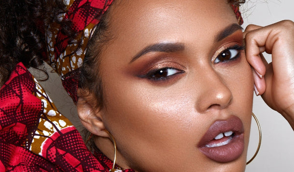 Nahaufnahme einer Frau mit warmem Smokey-Eye-Make-up, glänzender Haut, großen Creolen und gemustertem Kopftuch.