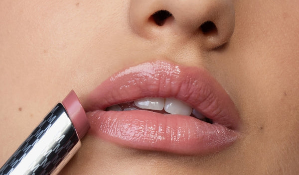 Nahaufnahme von Lippen, die mit rosiger, glänzender Lippenpflege direkt aus dem Stift aufgetragen wird.