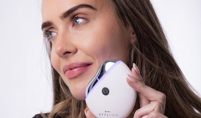 Frau verwendet ein elektrisches Gesichtsmassagegerät zur Lymphdrainage an ihrer Wange.