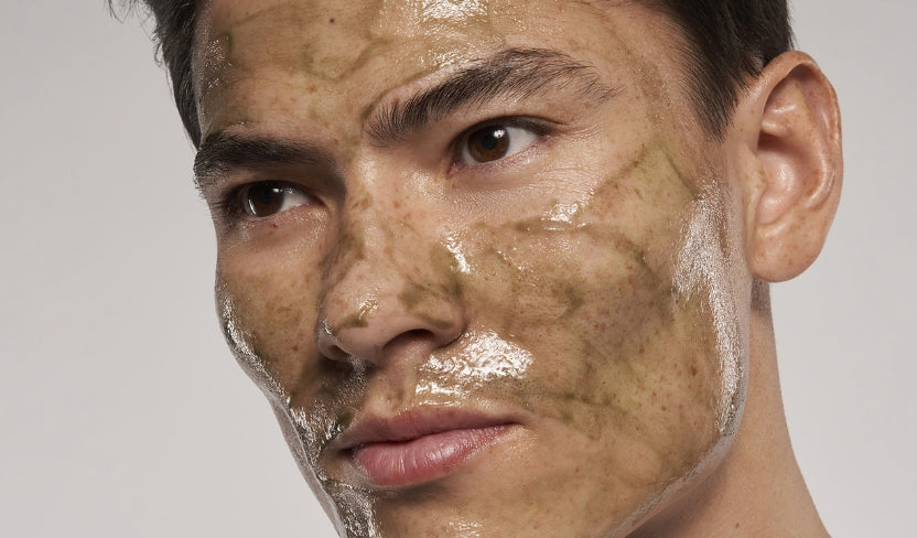 Mann mit braunen Augen und dunkeln Haaren trägt eine olivgrüne Gesichtsmaske.