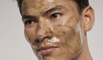 Mann mit braunen Augen und dunkeln Haaren trägt eine olivgrüne Gesichtsmaske.