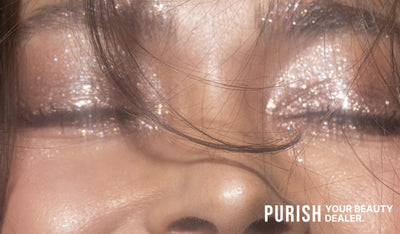 Nahaufnahme geschlossener Augen mit schimmerndem, glitzerndem Lidschatten, einzelne Haarsträhnen im Gesicht.