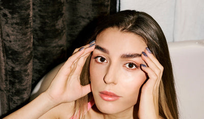 Frau mit glatten Haaren und natürlichem Make-up hält ihren Kopf mit beiden Händen und blickt direkt in die Kamera.