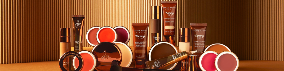 Frau mit Foundation-Swatches in verschiedenen Hauttönen auf der Wange vor rotem Hintergrund.