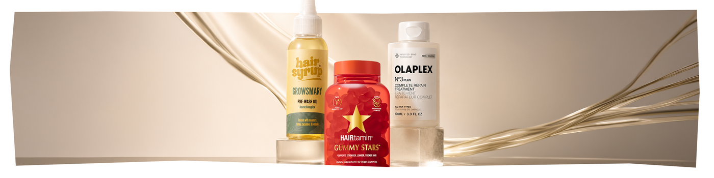 Eine Person in einem weißen Bademantel hält Shampoo, Spülung, eine Tube und eine violette Kopfhautbürste.
