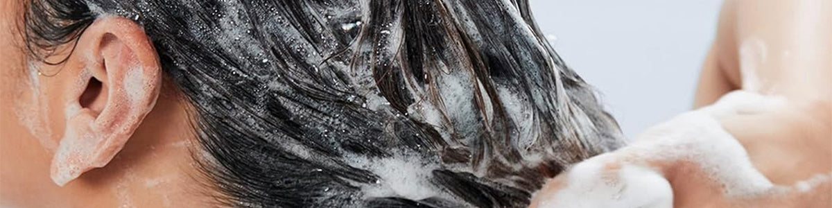 Nahaufnahme einer Person, die ihre Haare mit Shampoo wäscht, wodurch ein Schaum aus Blasen und Schaum entsteht.