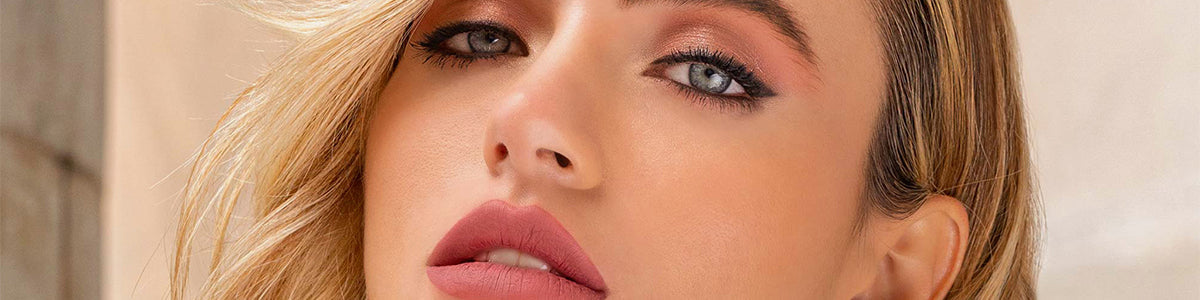 Nahaufnahme einer Frau mit welligem blondem Haar, rosa Lippenstift und schimmerndem Lidschatten, die in die Kamera schaut.