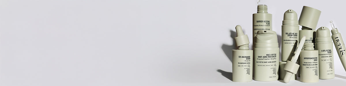 Eine Gruppe von beigen Hautpflegeflaschen und -tropfern, aufrecht angeordnet auf einem hellgrauen Hintergrund.