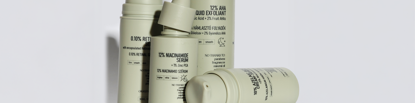 Eine Gruppe von beigen Hautpflegeflaschen und -tropfern, aufrecht angeordnet auf einem hellgrauen Hintergrund.